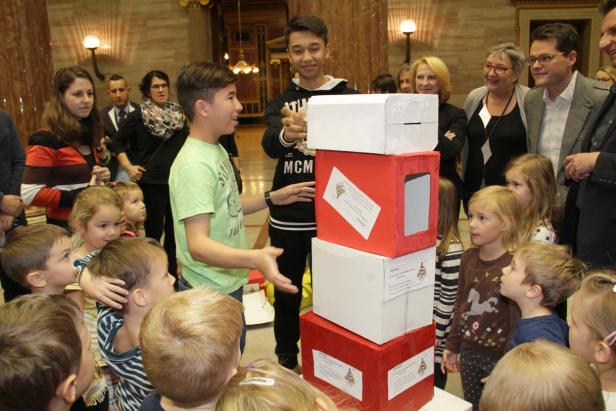 Eine Gruppe Kinder und Erwachsene betrachtet einen Turm aus rot-weißen Kartons.