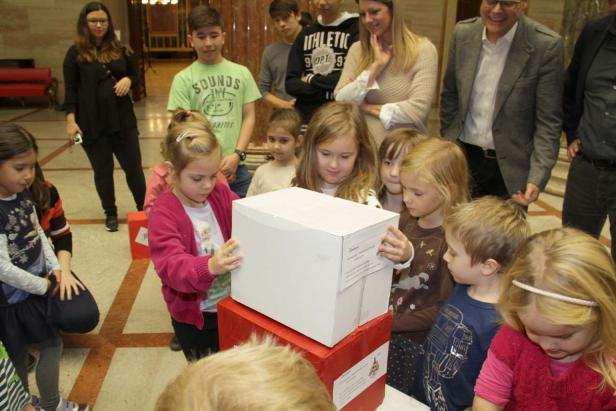Eine Gruppe Kinder steht um eine weiße Kiste in einem Raum.
