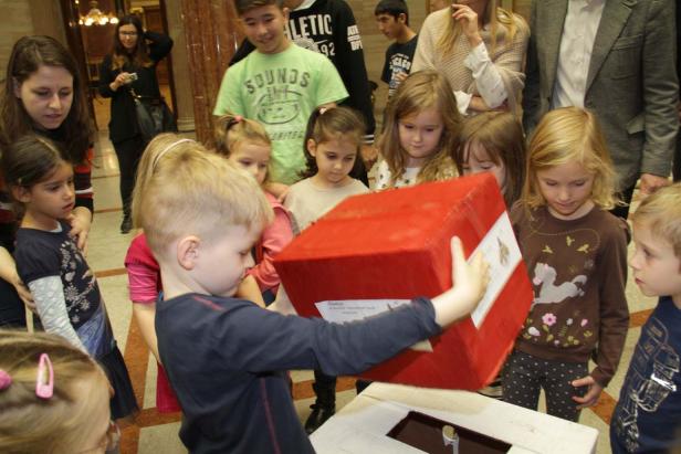 Eine Gruppe von Kindern betrachtet einen roten Würfel, der über eine Öffnung gehalten wird.