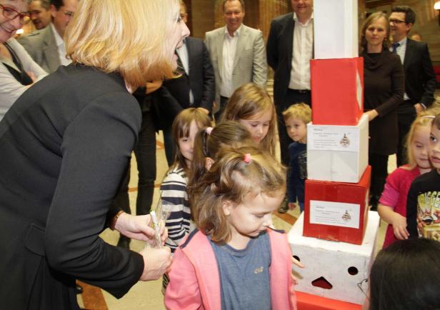 Eine Frau überreicht Kindern kleine Geschenke vor einem Stapel beklebter Kartons.