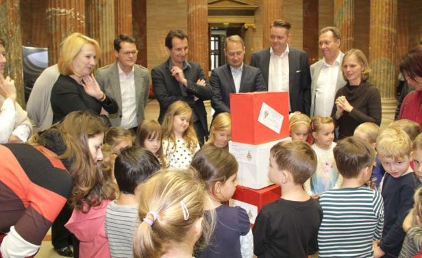 Eine Gruppe von Kindern und Erwachsenen steht um einen Stapel roter und weißer Kisten.