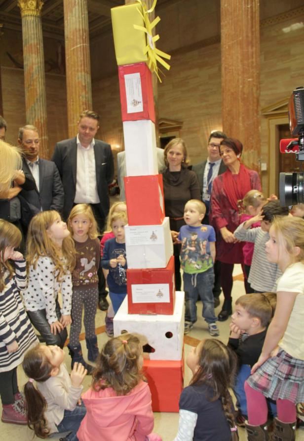 Eine Gruppe Kinder und Erwachsene steht um einen hohen Turm aus Geschenkboxen.