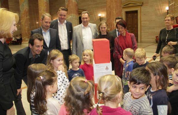 Eine Gruppe von Kindern und Erwachsenen steht um einen roten Kasten in einem großen Saal.