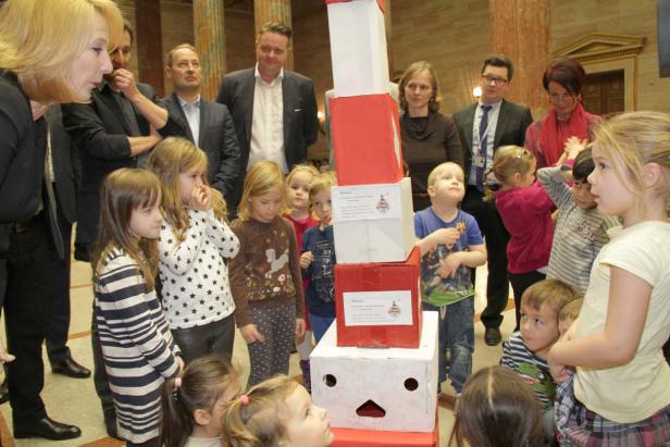 Eine Gruppe von Kindern und Erwachsenen steht um einen Turm aus roten und weißen Kartons.