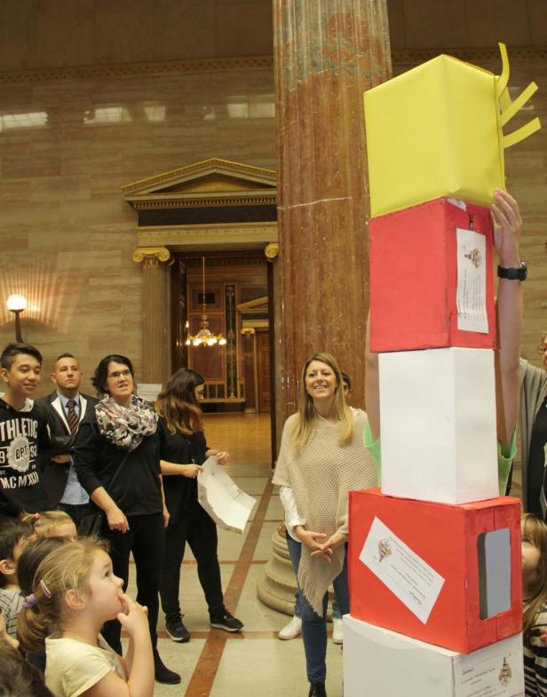 Eine Gruppe von Kindern und Erwachsenen steht um einen Turm aus bemalten Kartons.