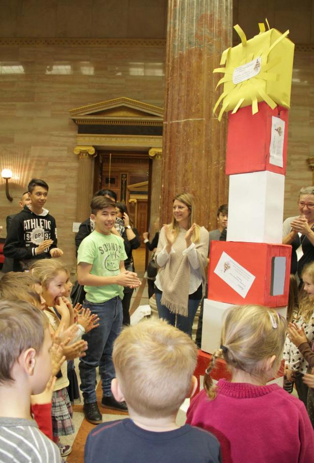 Eine Gruppe von Kindern und Erwachsenen klatscht vor einem Turm aus roten, weißen und gelben Kisten.