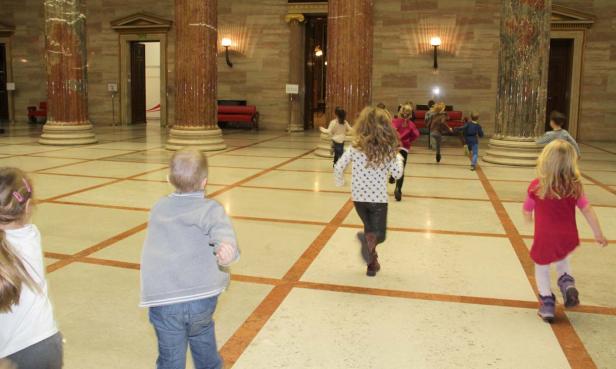 Eine Gruppe Kinder rennt in einer Halle mit Marmorsäulen herum.