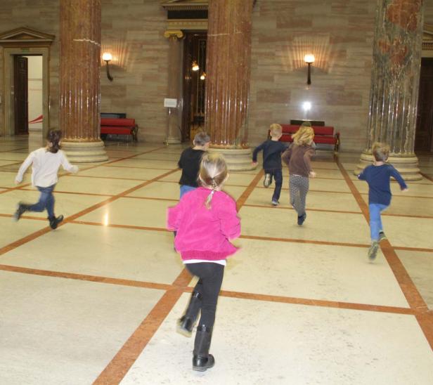 Eine Gruppe Kinder rennt in einer Halle mit Säulen herum.