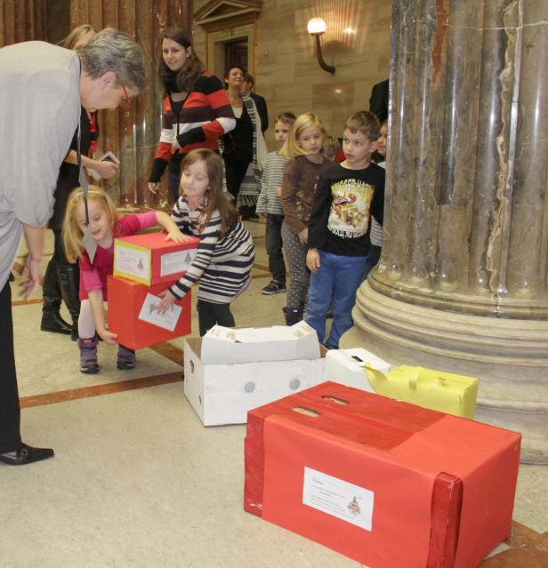 Eine Gruppe Kinder hantiert mit bemalten Kartons in einem Innenraum.