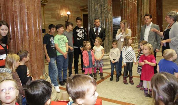 Eine Gruppe von Kindern und Erwachsenen steht in einem Raum mit Marmorsäulen.