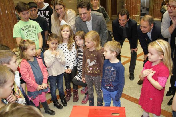 Eine Gruppe von Kindern und Erwachsenen steht in einem Raum mit Säulen.