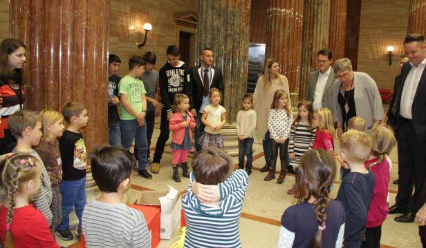 Eine Gruppe von Kindern und Erwachsenen steht in einem Raum mit Marmorsäulen.