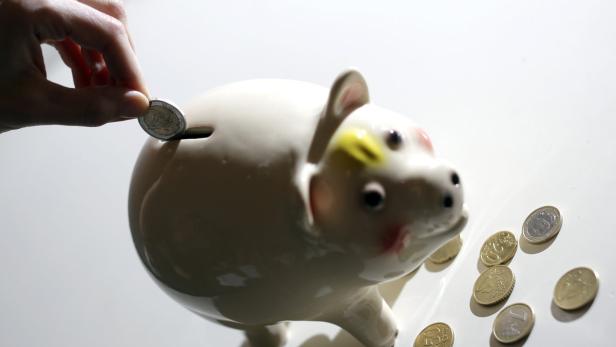 Eine Hand wirft eine Zwei-Euro-Münze in ein Sparschwein.