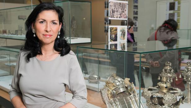 Eine Frau steht vor Vitrinen mit historischen Silberobjekten in einem Museum.