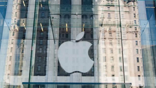 Das Apple-Logo ist an einem Gebäude angebracht, das sich in den Glasscheiben spiegelt.
