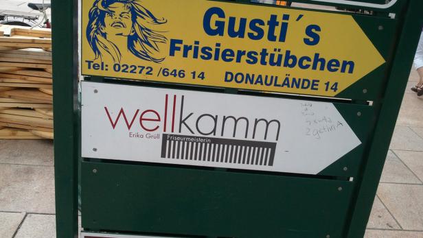 Ein Wegweiser zeigt zu „Gusti’s Frisierstübchen“ und „wellkamm Erika Grüll Friseurmeisterin“.