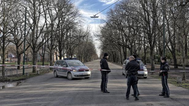 Polizisten sichern eine Straße mit Polizeiautos und Absperrband ab.