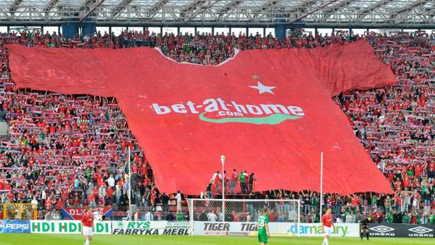 Fußballfans halten ein riesiges Trikot mit der Aufschrift „bet-at-home.com“ im Stadion hoch.