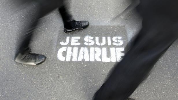 Füße laufen über den Schriftzug „Je suis Charlie“ auf dem Asphalt.
