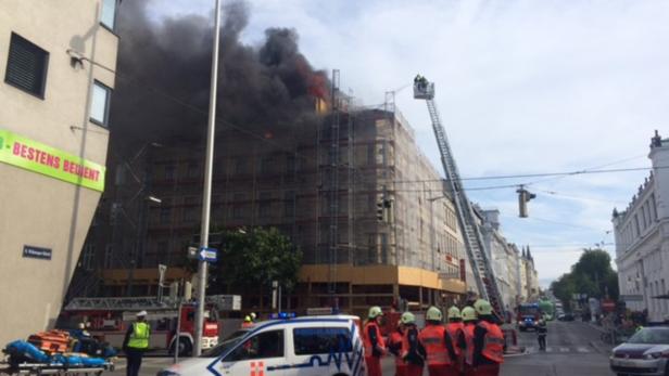 Ein Gebäudebrand in einer Stadt, mit Feuerwehrleuten auf einer Drehleiter und Rettungskräften am Boden.