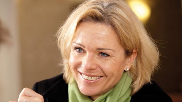Eine lächelnde Frau mit blonden Haaren und einem grünen Schal.