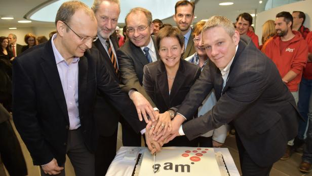 Eine Gruppe von Personen schneidet gemeinsam eine Torte mit dem Logo „sam“ an.