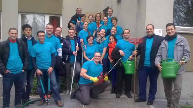 Eine Gruppe von Freiwilligen in blauen T-Shirts posiert mit Gartengeräten für ein Foto.