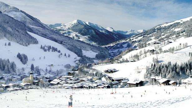 Ein verschneites Dorf in den Bergen mit vielen Skifahrern auf der Piste.