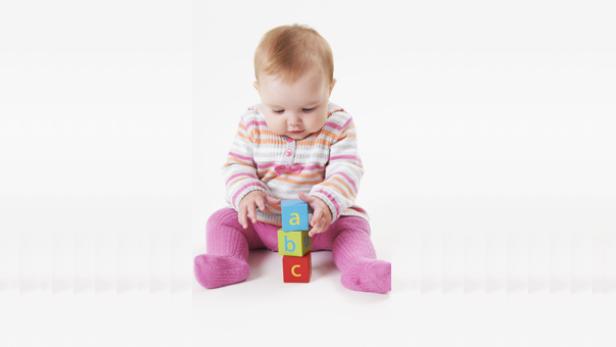 Ein Baby sitzt und spielt mit Bauklötzen, auf denen die Buchstaben A, B und C stehen.
