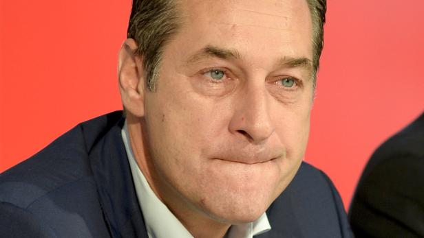 Nahaufnahme eines Mannes in einem dunklen Anzug vor einem roten Hintergrund.