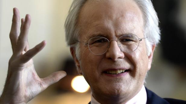 Ein Mann mit Brille lächelt und hebt seine Hand.