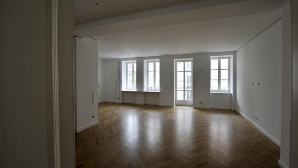Ein leerer Raum mit Parkettboden und weißen Wänden mit drei Fenstern.