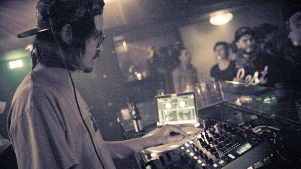 Ein DJ legt in einem Club vor Publikum Musik auf.