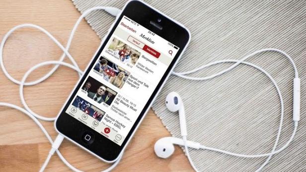 Ein Smartphone mit Kopfhörern liegt auf einem Tisch und zeigt eine App mit verschiedenen Videoinhalten.