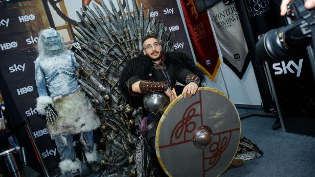 Ein Mann im Kostüm sitzt auf dem Eisernen Thron neben einem Charakter aus „Game of Thrones“.