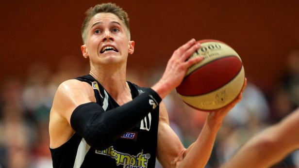 Ein Basketballspieler mit Ball in der Hand blickt angespannt nach oben.
