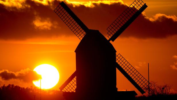 Die Silhouette einer Windmühle vor einem orangefarbenen Sonnenuntergang.