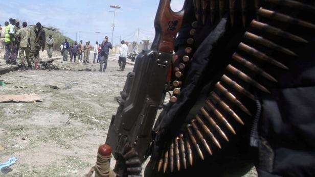 Ein bewaffneter Mann steht vor einer Gruppe von Menschen und Trümmern.