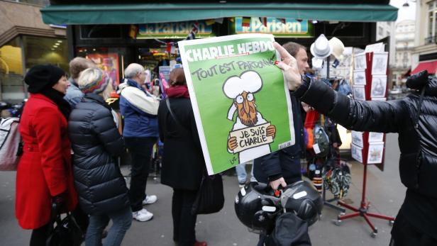 Eine Person hält eine Ausgabe von „Charlie Hebdo“ mit der Aufschrift „Je suis Charlie“ in die Höhe.