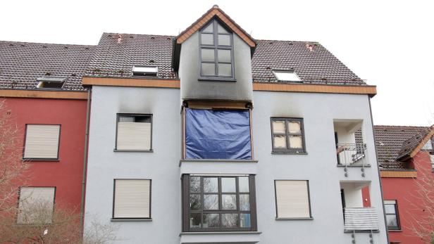 Ein Wohnhaus mit Brandschäden an mehreren Fenstern, eines davon mit einer blauen Plane abgedeckt.