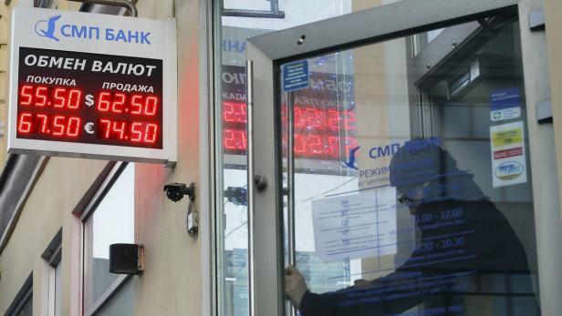 Ein Mann betritt eine Bankfiliale, an der eine Wechselkurstafel hängt, die Dollar- und Eurokurse anzeigt.