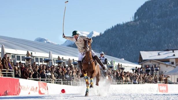 Ein Polospieler reitet auf einem Pferd durch den Schnee und schwingt einen Schläger.