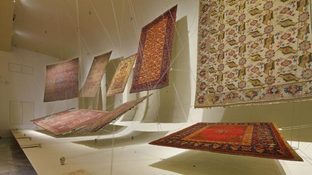 Mehrere Teppiche hängen an Seilen in einer Kunstausstellung.