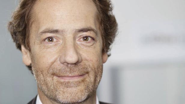 Porträt eines Mannes mit braunen Haaren und Bart vor einem hellen Hintergrund.