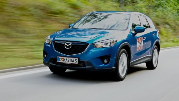 Ein blauer Mazda CX-5 fährt auf einer Landstraße.