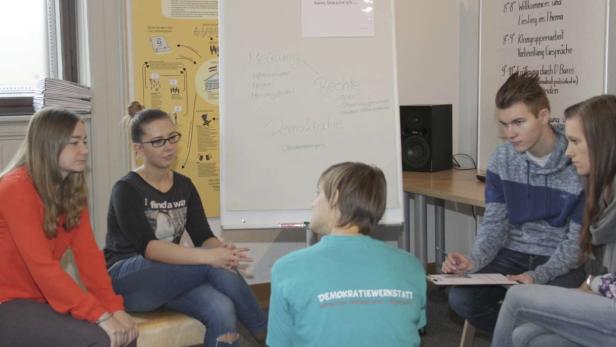 Eine Gruppe junger Leute sitzt im Kreis und diskutiert über Demokratie.