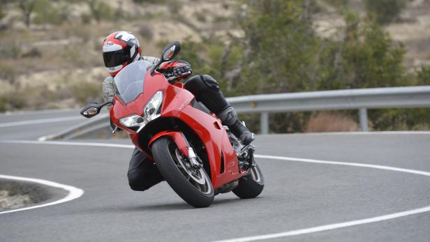 Ein Motorradfahrer fährt mit einer roten Honda VFR auf einer kurvenreichen Straße.