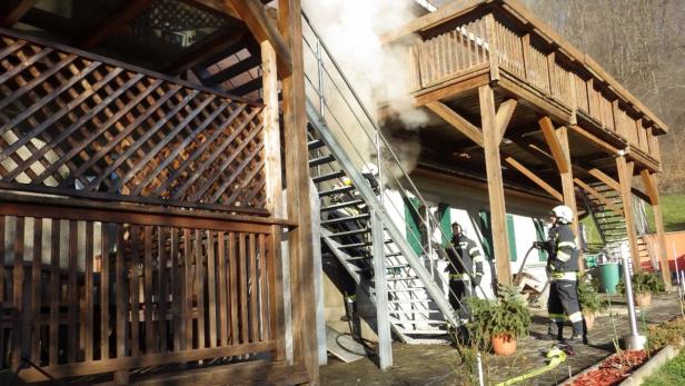 Feuerwehrleute stehen vor einem Haus, aus dem Rauch dringt.