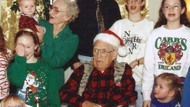 Eine Gruppe von Menschen, darunter ein älterer Mann mit Weihnachtsmütze im Rollstuhl, posiert für ein Foto.