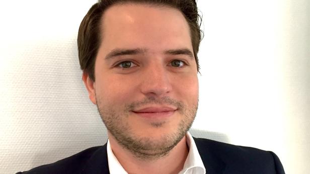 Ein Mann mit dunklen Haaren und Anzug lächelt in die Kamera.